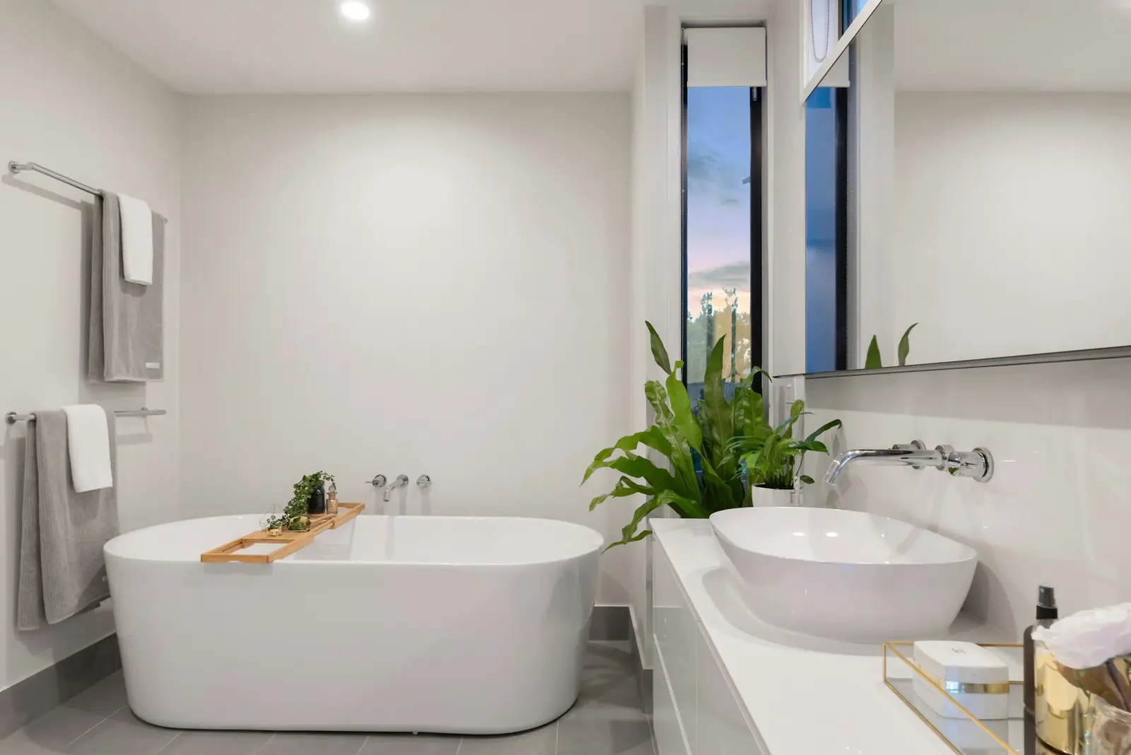 Bright white fitted bathroom with freestanding bath, vessel basin and plants