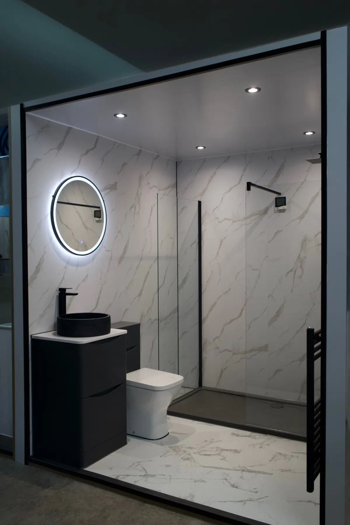 Showroom bathroom with marble-effect panels, black vessel basin and round LED mirror